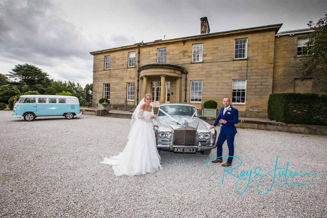 Bride and groom stood outside Saltmarshe Hall with a glass of champagne and their wedding cars