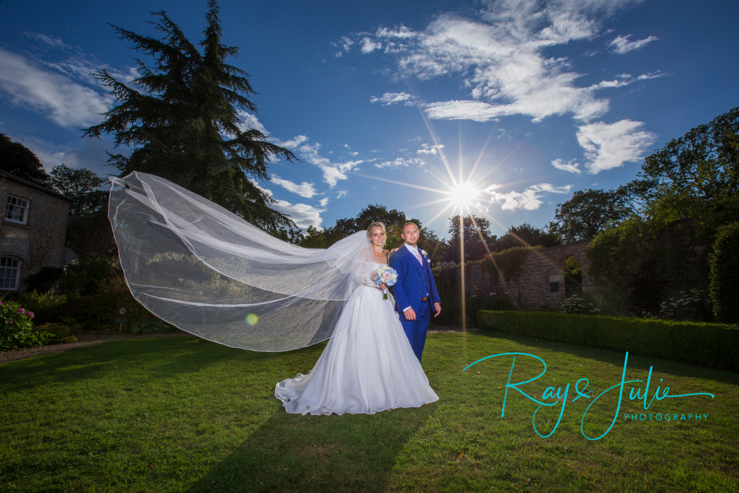 Bride with veil blowing and Groom looking very smart. With bright sunburst taken in the grounds at Saltmarshe Hall.