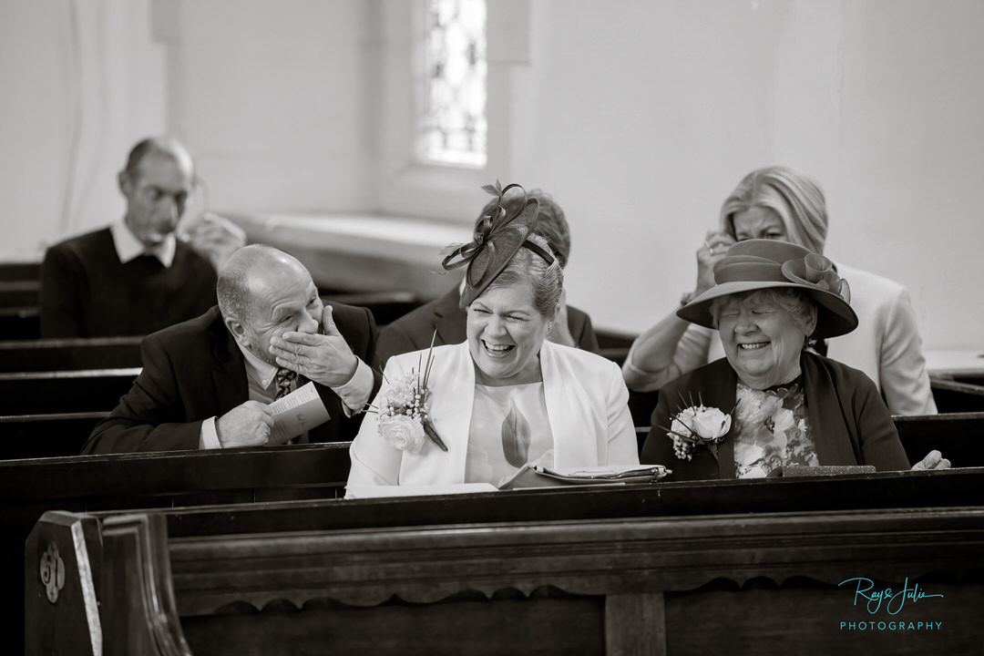 Wedding guests sharing a joke in church prior to the service. Black and white