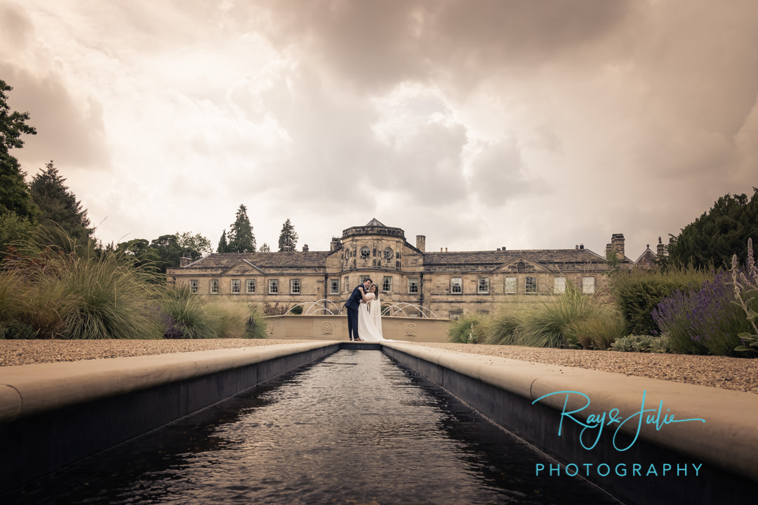 Wedding couple embrace Grantley Hall and water fountain behind them