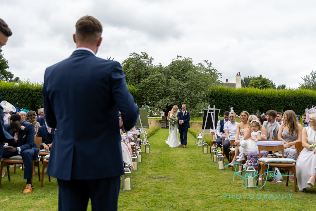 Bride and dad walking to onlooking groom, at their outdoor wedding ceremony at Tickton Grange