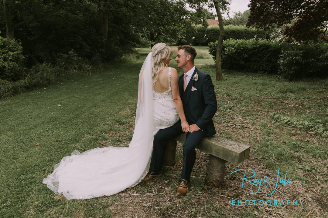 Bride and Groom sat on a bench looking at each other. Outdoor summer wedding photograph captured at Tickton Grange East Riding of Yorkshire.