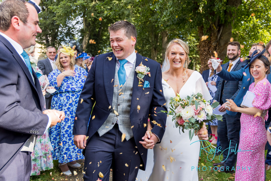 Bride and groom walking and smiling whilst confetti is being thrown over them
