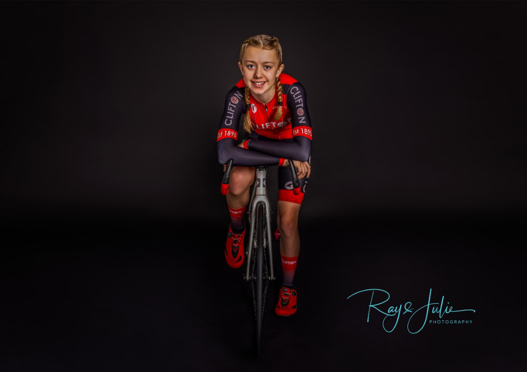 Young cyclist in a red and black outfit poses on a bike against a dark background. Text on the image reads "Roy & Julie Photography.