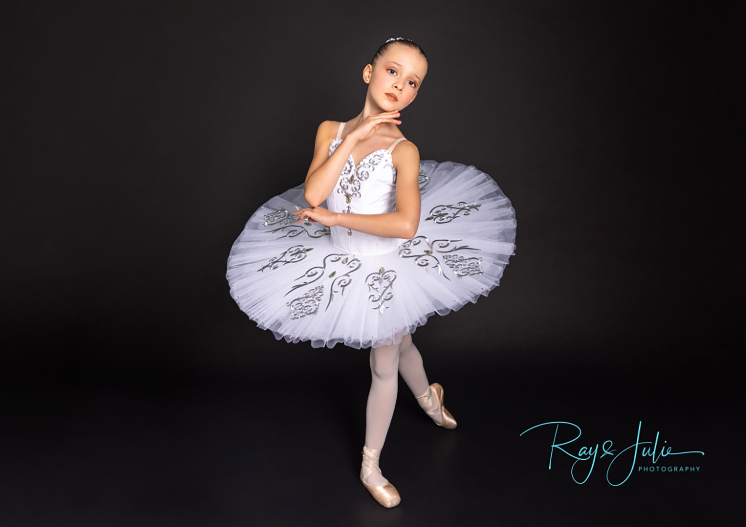 Young ballet dancer in a white tutu poses gracefully against a dark background.