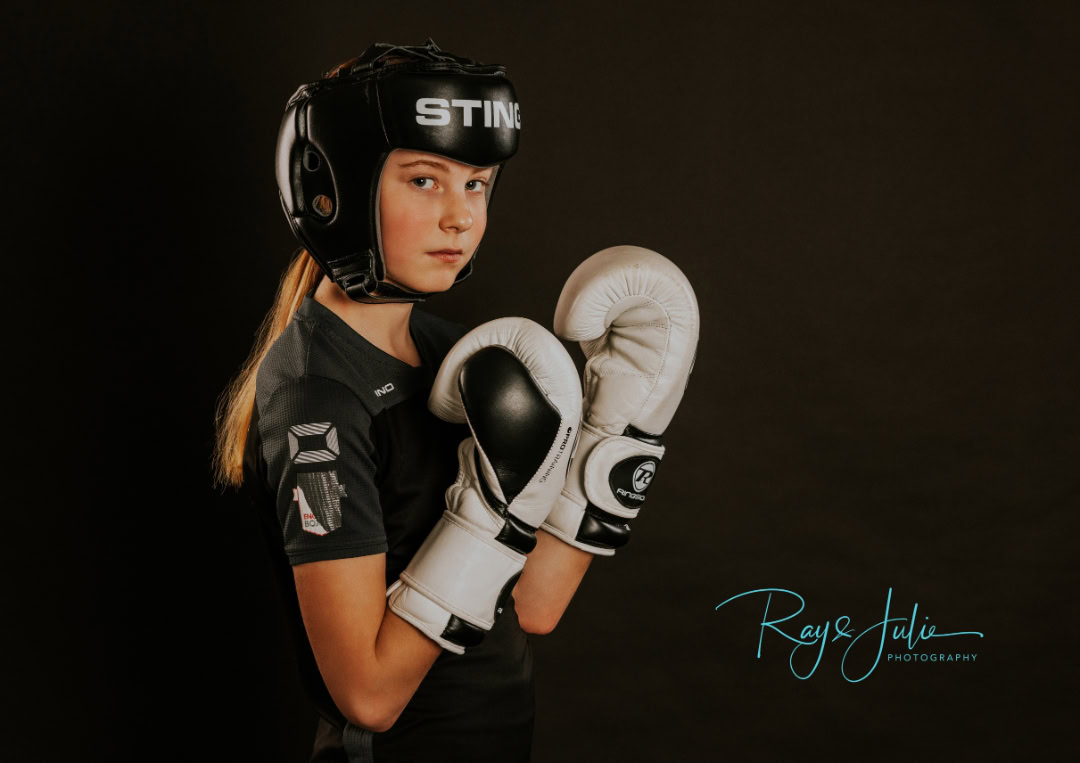 Young person wearing a black helmet and gloves in a boxing stance against a dark background.