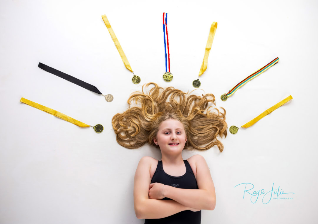 Girl lying on her back with her hair fanned out. Several medals are arranged around her head on a white background.