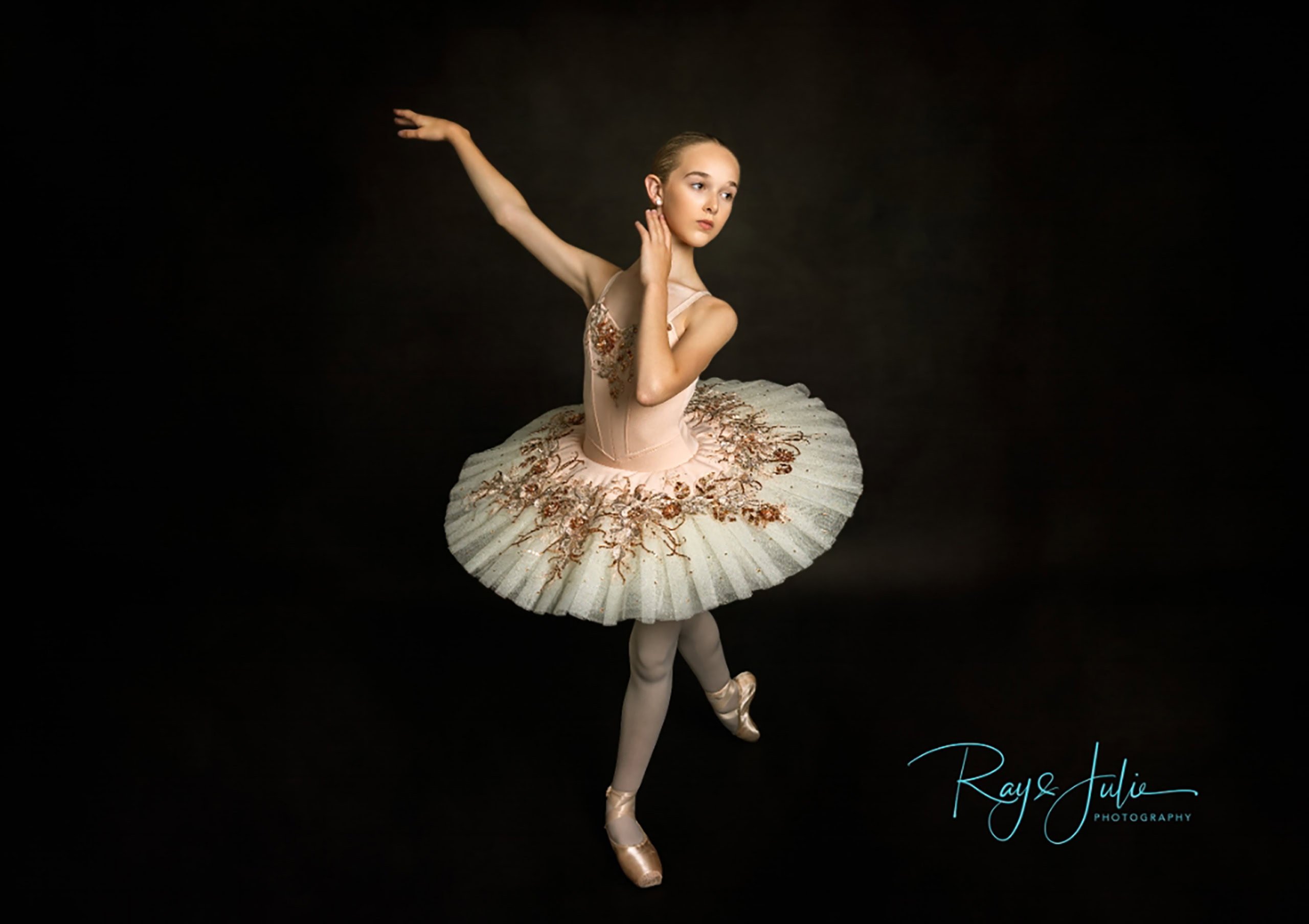 Ballerina in a posed position wearing a decorated white tutu, photographed against a dark background.