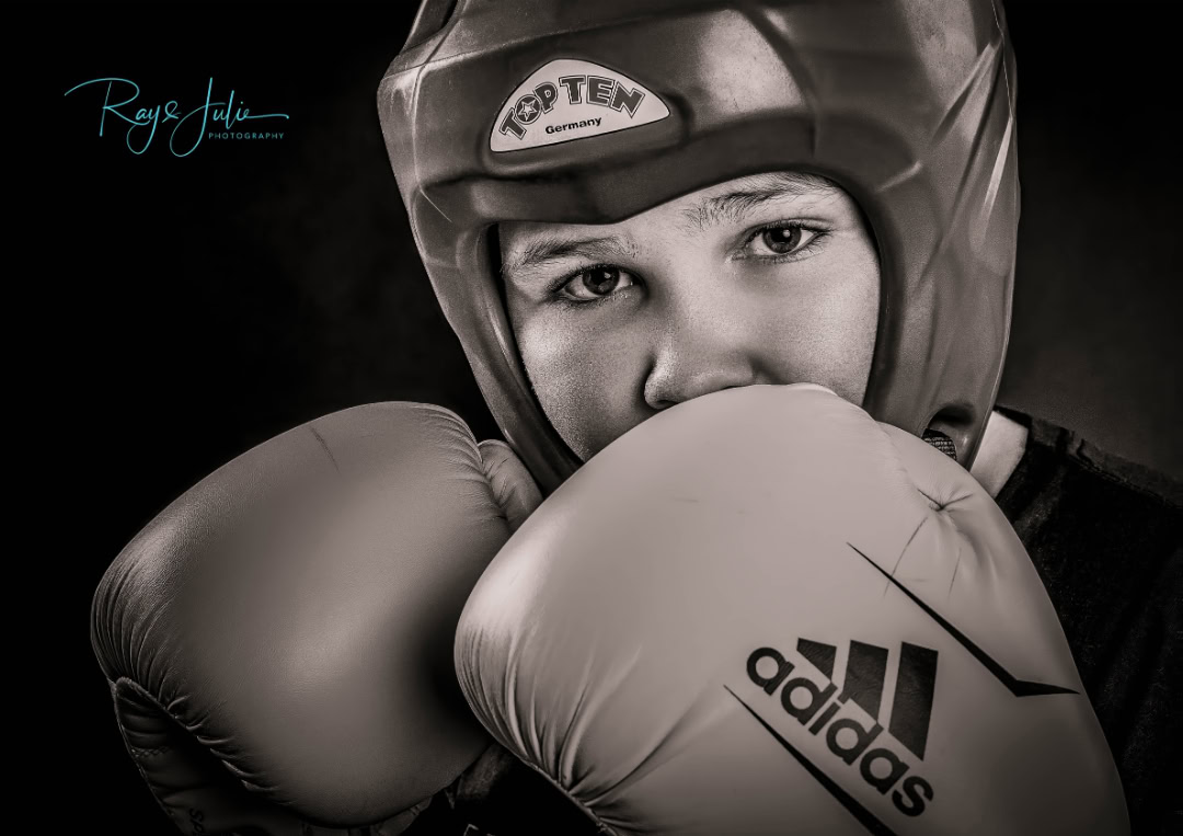 A child wearing a boxing helmet and gloves, looking into the camera. The helmet has "Top Ten Germany" on the front, and the gloves have the Adidas logo.